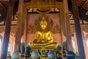 The background of the Wat Pa Kham Charoen is a beautiful old church with a Buddhist statue and a tree-lined temple, with tourists and travelers always making merit in Udon Thani, Thailand.