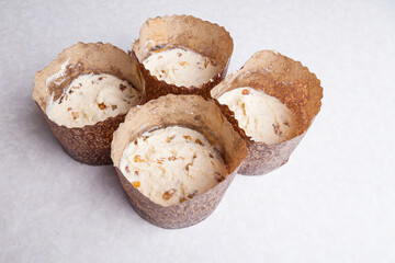 Four tins for baking muffins at home made of brown cooking paper filled with raw raisin dough on a white table. Home hobby baking Easter cakes.