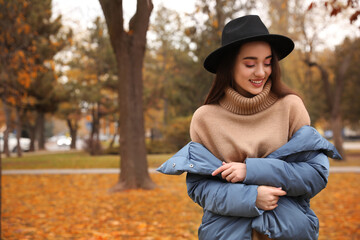 Young woman wearing stylish clothes in autumn park, space for text