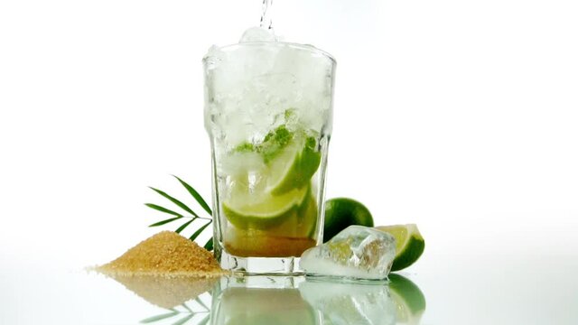 Pouring Cachaca in a Caipirinha Cocktail on white Background - Lime and brown Sugar