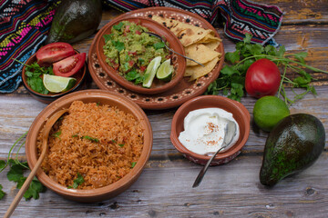 Traditional mexican rice, guacamole, corn tortillas on wooden background