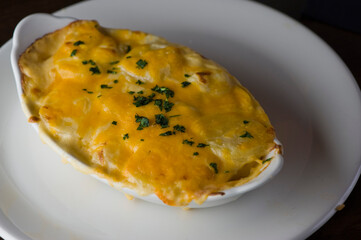 Potatoes au gratin. Potatoes baked in butter, cheese cream sauce, garnished with scallions, parsley and served in cast iron skillet. Classic American restaurant or French bistro side dish.