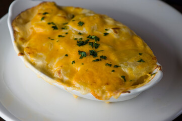 Potatoes au gratin. Potatoes baked in butter, cheese cream sauce, garnished with scallions, parsley and served in cast iron skillet. Classic American restaurant or French bistro side dish.