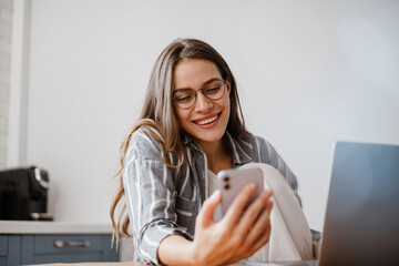 Joyful beautiful woman using cellphone while sitting at table