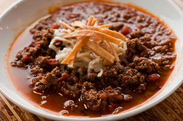 Chili—Texas style five alarm chili. Ground beef seasoned with peppers, spices, onions, slow cooked and served with cheddar cheese and crispy fried tortillas. Traditional southern cooking cuisine.