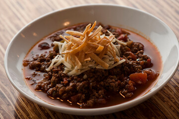 Chili—Texas style five alarm chili. Ground beef seasoned with peppers, spices, onions, slow cooked and served with cheddar cheese and crispy fried tortillas. Traditional southern cooking cuisine.