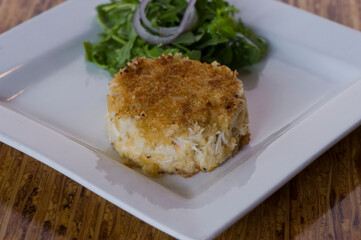 Crab cake. Crab served with spicy rémoulade sauce on top of a mixed green salad. Jumbo crab meat mixed with garlic, onions, spices & fried in butter. Classic American restaurant appetizer.