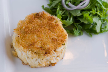 Crab cake. Crab served with spicy rémoulade sauce on top of a mixed green salad. Jumbo crab meat mixed with garlic, onions, spices & fried in butter. Classic American restaurant appetizer.