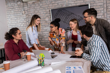 Group of modern business people in casual wear discussing architectural designs while sitting in the creative office.