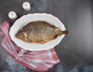 Grilled fish carp on a white plate against a dark background. Copy space