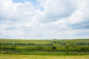 Summer rural landscape with cloudy sky. Nature untouched by man, green hills far from cities. Rural countryside, field overgrown with grass, background
