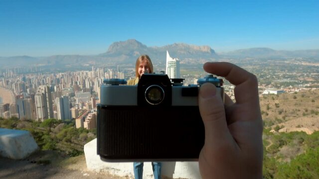 Interesting video concept of creative content creator make photos of happy tourist smiling young woman on top of travel spot though viewfinder of vintage film analog camera. POV travel blogger concept