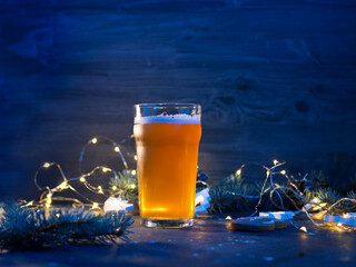 A glass of Christmas beer ginger ale on the festive table at night with garlands and branches of...