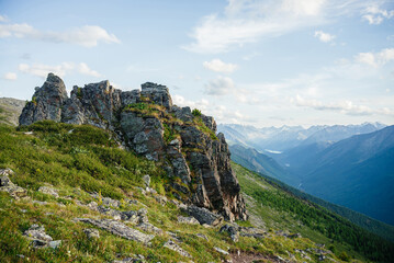 Scenic mountain landscape with great sharp rock on hillside. Awesome alpine scenery with beautiful pointy crag on background of snowy mountains under blue sky. Big pointed stone on mountainside.