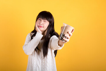 Portrait of lovely asian woman holding pearl milk tea. Asian exotic beverage concept. Studio shot isolated on yellow background.