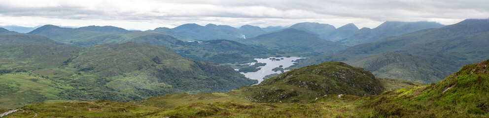 Fototapeta na wymiar Panoramic view of the Irish countryside with trees, green vegetation and lakes with mountains and hills, cloudy day in Ireland