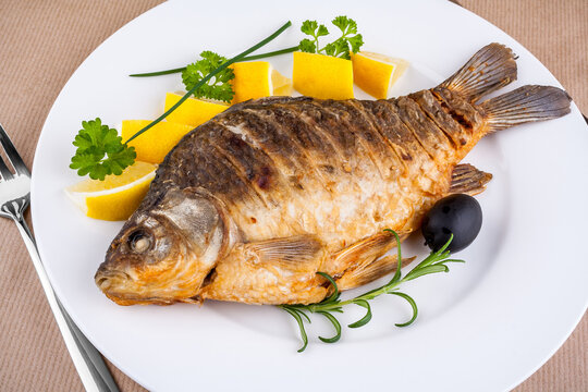 Fried fish on white plate with fork and knife