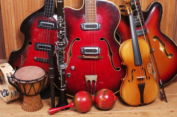 Fototapeta na wymiar Three vintage electric guitars, violin with bow, clarinet, maracas, djembe on a wooden floor.