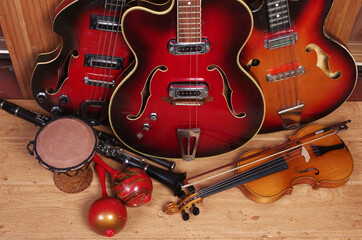Fototapeta na wymiar Three vintage electric guitars, violin with bow, clarinet, maracas, djembe on a wooden floor.