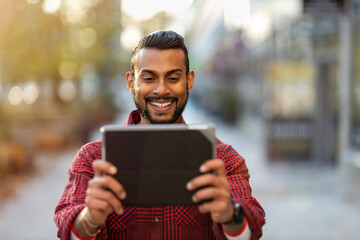 Smiling young man using tablet outdoors at urban setting
