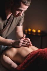 Male masseur doing back massage to client woman in dark room of massage spa