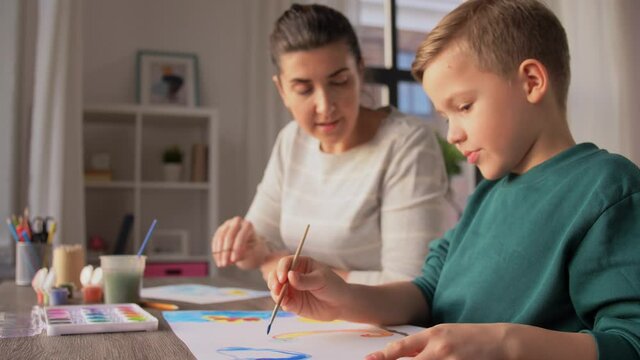 family, leisure and people concept - mother and little son with colors and paper drawing at home and making high five gesture