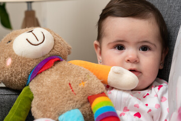 Close-up of happy baby girl playing with cute colourful teddy