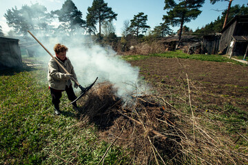 An old woman burns branches near the house on her farm in the village.