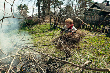 Old woman burns branches near the house on her farm.