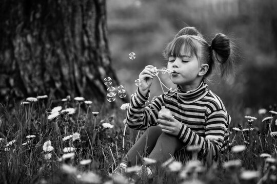 Naklejki Little cute girl blowing soap bubbles in the park. Black and white photo.