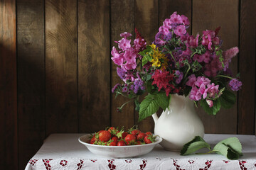 bouquet of pink Phlox and purple ageratum in a white jug and strawberries.