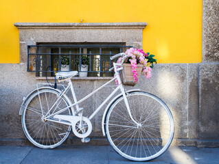 Fototapeta na wymiar Stylish white bicycle with a basket full of flowers leaning against a yellow wall in the streets of Porto, Portugal