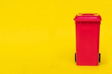 red wheelie waste bin on yellow background.