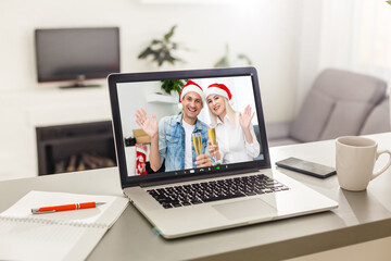 couple waving while having a videocall in santa hats on laptop at home. social distancing during christmas festivity quarantine lockdown concept.