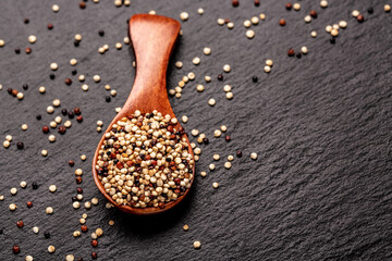 mixed raw unprocessed quinoa seed in wooden scoop on a stone background. superfood product. banner,...