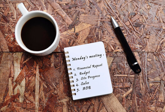 Monday meeting list text on note pad with background of cup of coffee and a pen