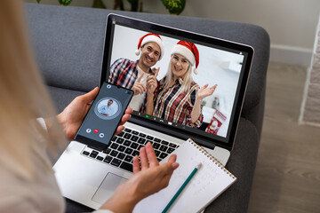Fototapeta na wymiar couple waving while having a videocall in santa hats on laptop at home. social distancing during christmas festivity quarantine lockdown concept.