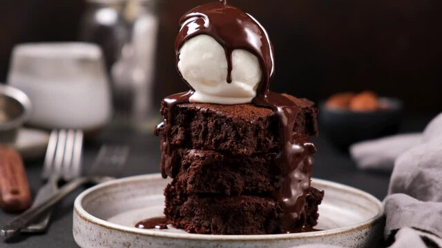 Chocolate brownies with vanilla ice cream and chocolate syrup. Syrup pouring on ice cream on brownies. Rich in sugar high calorie sweet food