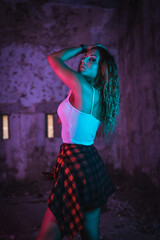 Lifestyle, portrait of a young Caucasian woman in a pose, wearing a tight white shirt and a plaid shirt at the waist. Pink and blue neon lights, urban photography