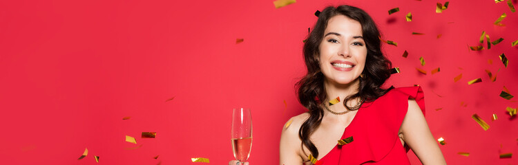  woman holding glass of champagne under falling confetti on red background, banner