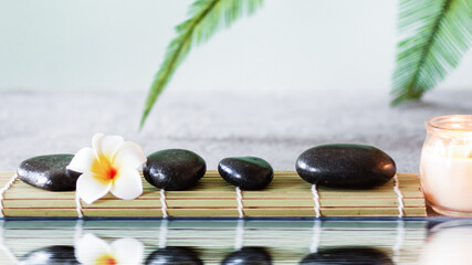 Black zen stones on grey concrete background with palm leaf near water with reflection.