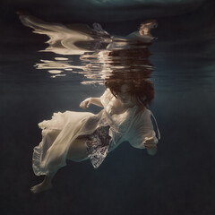 A girl in a light fluttering dress swims underwater as if floating in weightlessness against a dark background