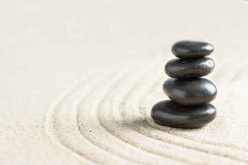 Black zen stones in a stack on beach sand. Meditation stone background.