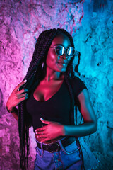 Black girl with long braids, sunglasses and a black T-shirt. Portrait with pink and blue neon lights