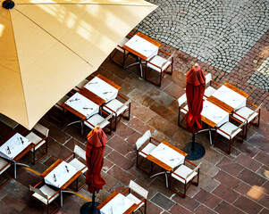 An overhead view of the empty tables and umbrellas of a street cafe in front of the cathedral in the tourist center of Strasbourg. - 395352113