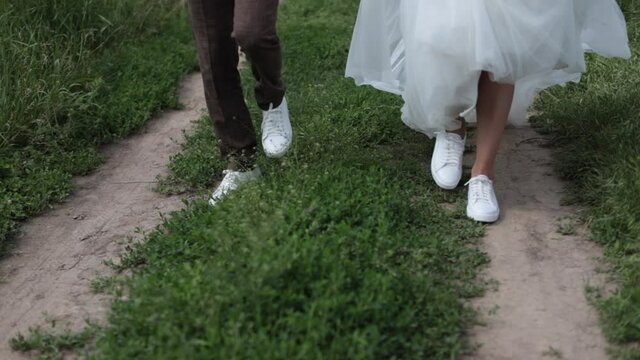 The bride and groom are walking in sneakers across the field. High quality FullHD footage