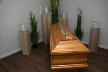 Ein Eichensarg steht in der Trauerhalle, Kerzen brennen.