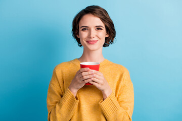 Photo of sweet cute lady wearing casual yellow sweater holding red cup hands arms isolated blue color background