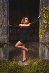 Lifestyle, Caucasian girl with wavy hair in a tight black dress and black high heels. Relaxed an abandoned place full of nature looking to the right