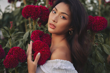 closeup portrait of a beautiful young Thai woman surrounded by red flowers. Spring blossom